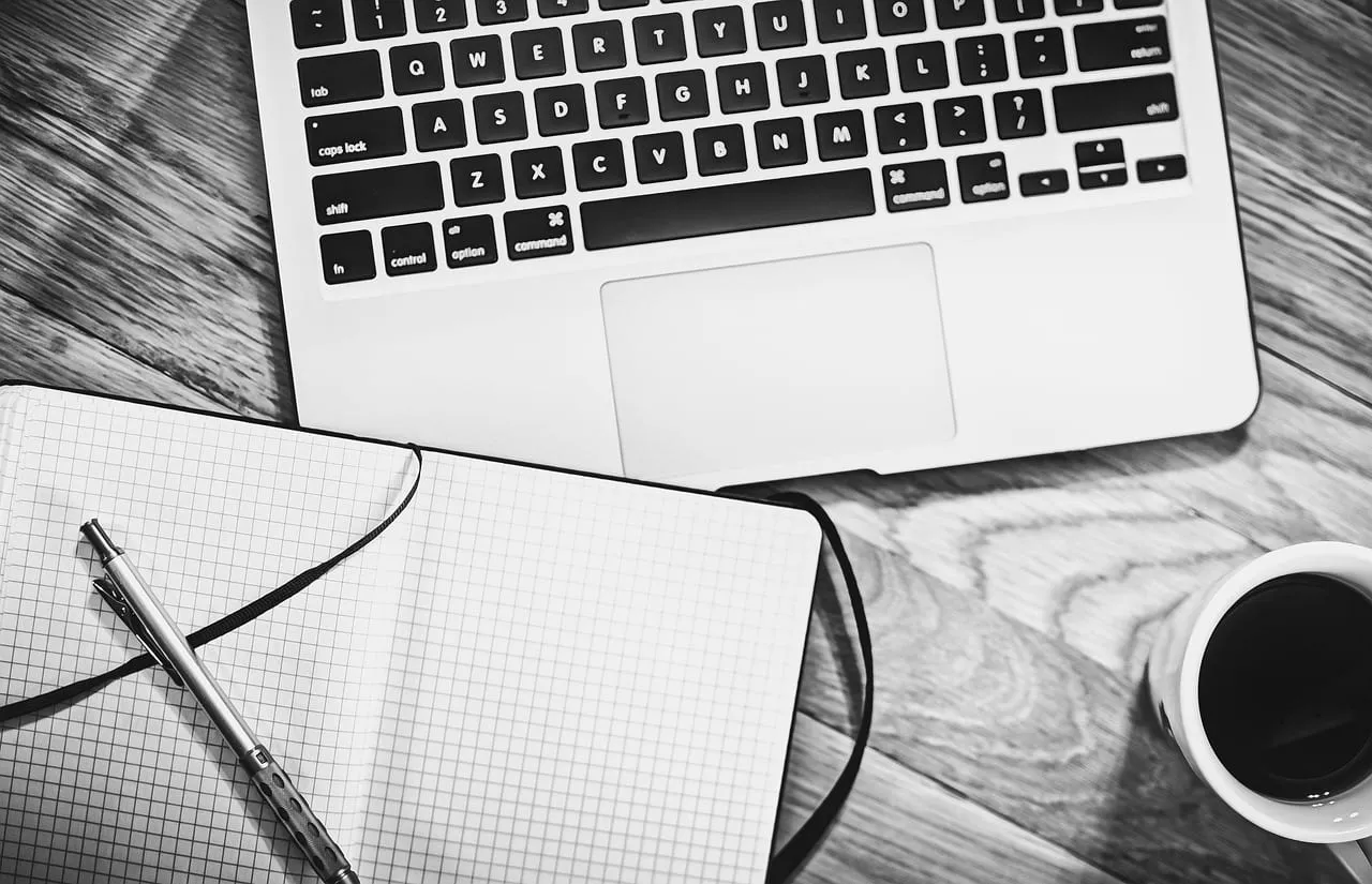 Photo showing computer, notebook, coffee and workspace.