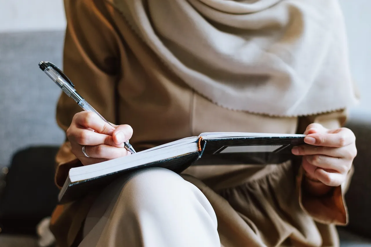 Photo showing muslim, woman, writing and notebook.